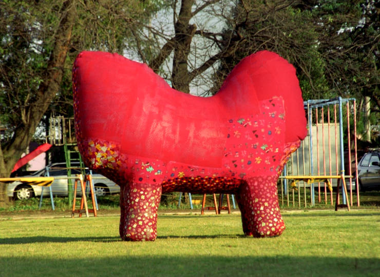 Robust, bright red, four-legged animal body like sculpture by Arunkumar H.G. displayed in a garden