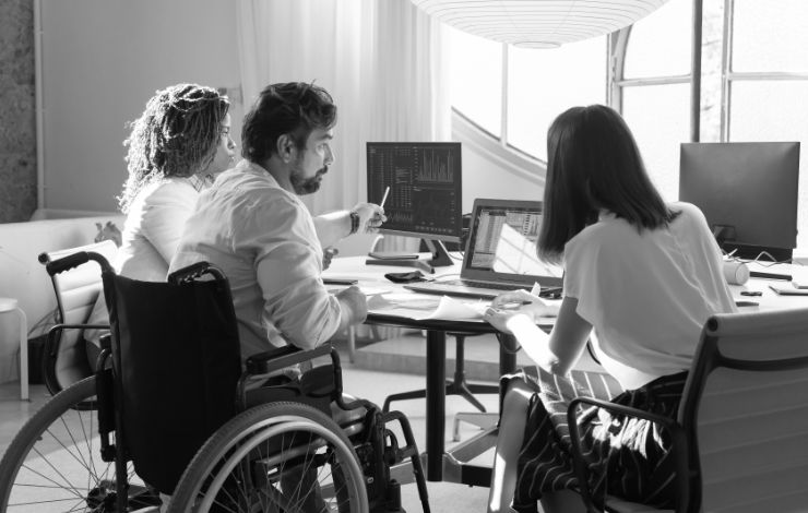 Man on a wheelchair working in an office, alongwith two colleagues