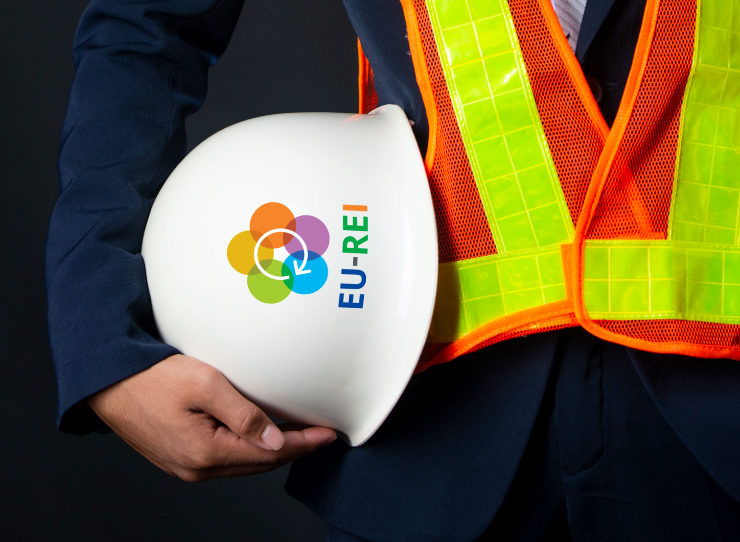 Man wearing a safety vest, carrying a safety helmet with the EU-REI logo printed on it