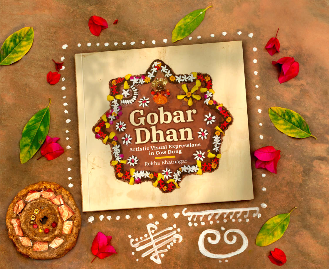The book, placed on the ground, surrounded by leaves, flowers and traditional Indian floor designs