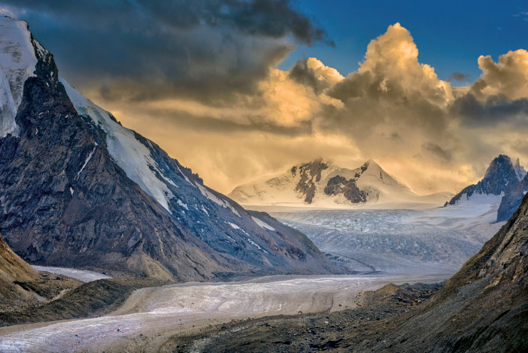 Valley of snow-covered, rocky hills with clouds lit up by the sun in the background