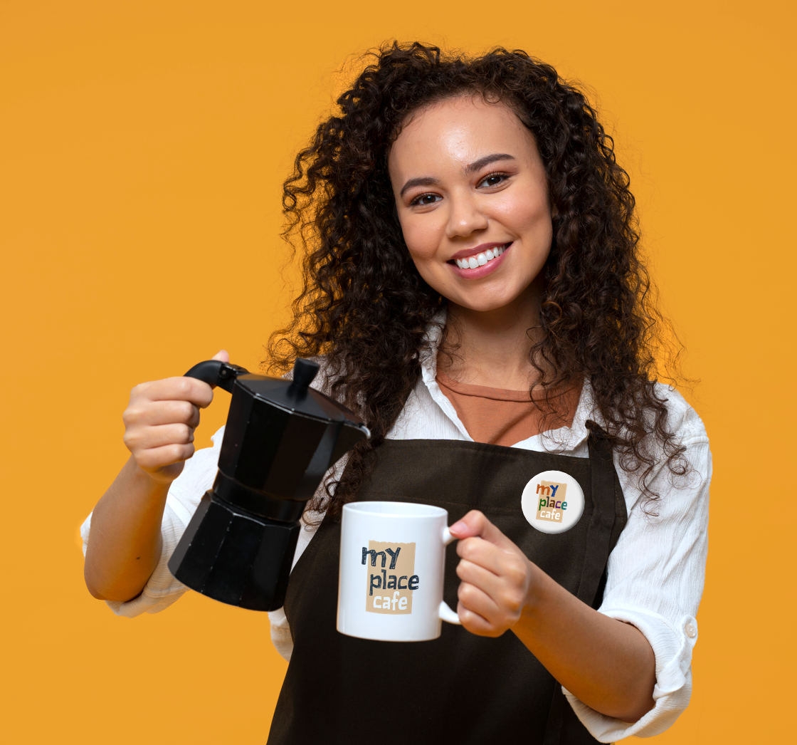 A barista wearing a My Place Cafe badge pouring coffee in a cup with the cafe logo on it