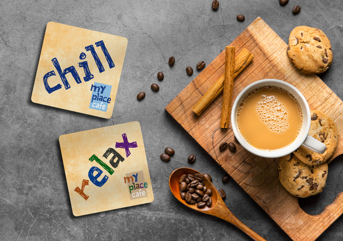 Two coasters with ‘Chill’ and ‘Relax’ written in logo font along with the logo, placed on a table with a cup of coffee