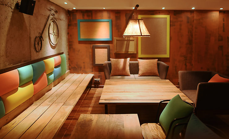 A cafe corner showing use browns, beige wooden planks, and bright coloured cushions on the seats