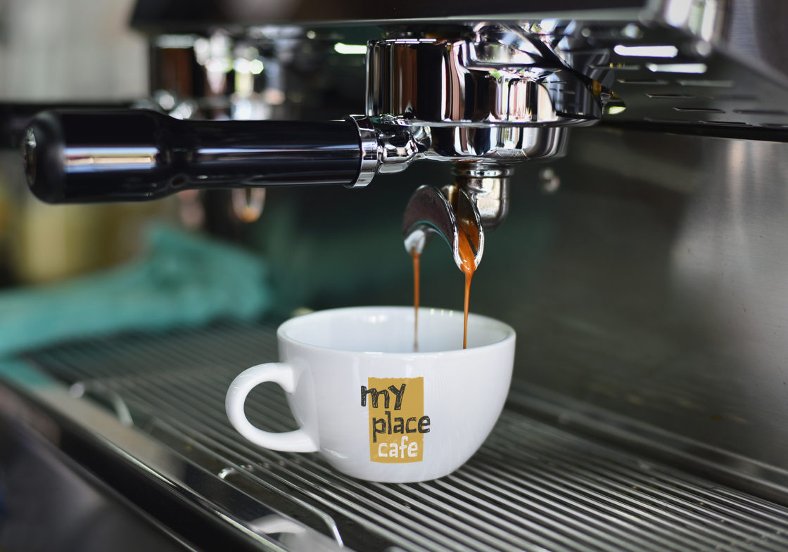 The logo printed on a coffee cup, placed below a coffee brewing machine