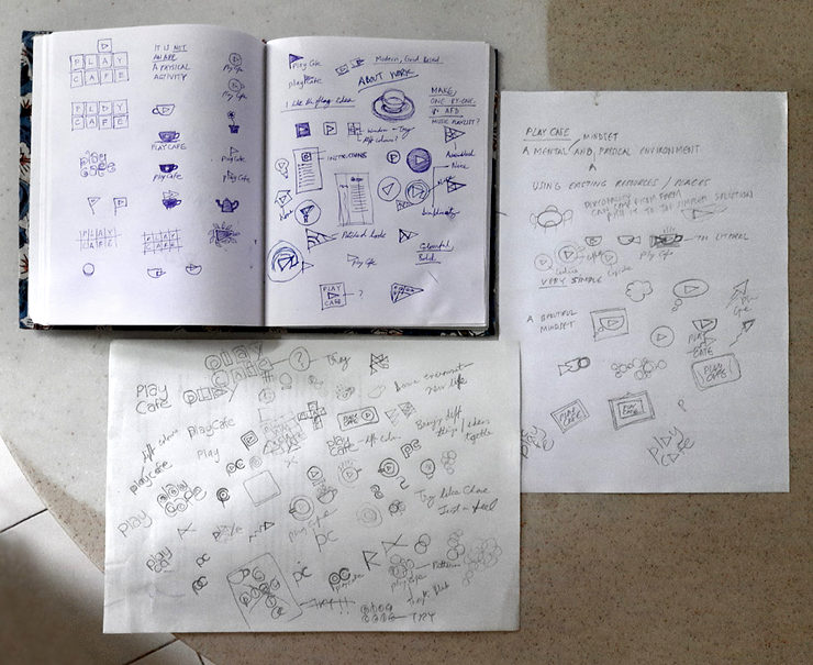 Pages of a sketch book and two loose sheets of papers filled with small, rough logo sketches