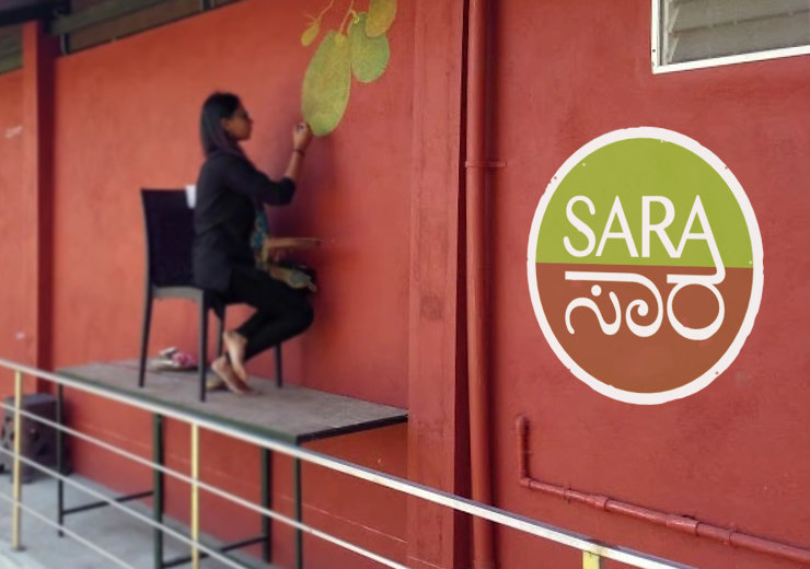 An artist making a painting on a wall, adjacent to a large SARA Centre logo