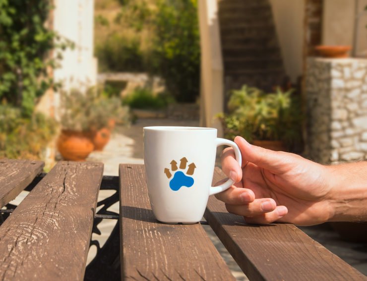 A coffee cup, placed on an outdoor wooden table, held by a man