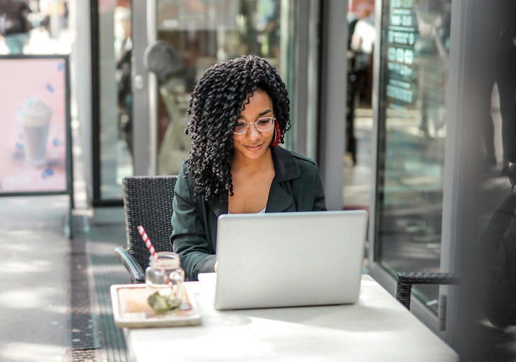 A woman working on an outdoor table of a coffee shop, with a drink on the side